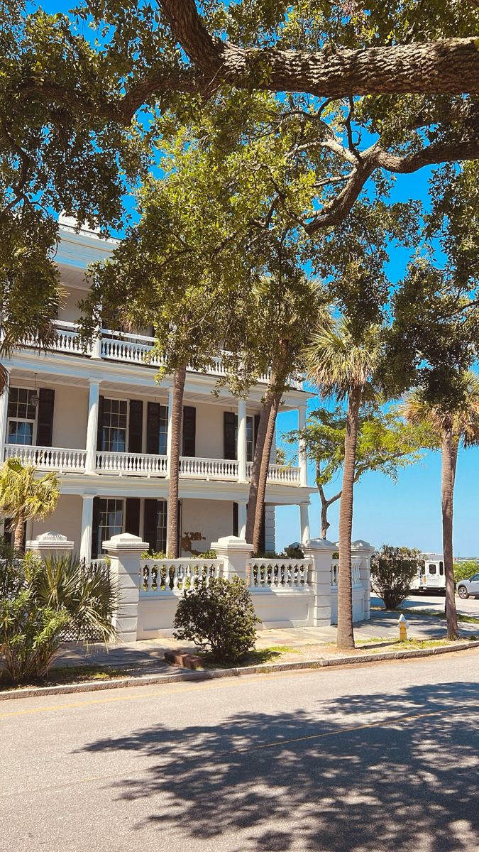 a large white building with balconies and trees on the sidewalk in front of it