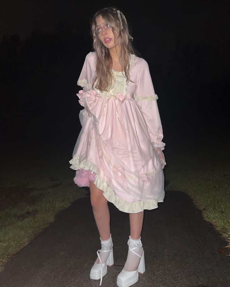 a girl in a pink dress and white shoes is standing on a path at night