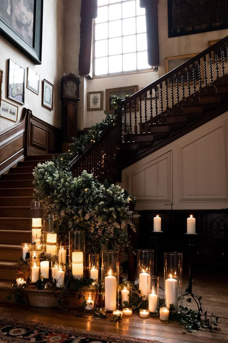 candles are lit on the floor in front of an ornate staircase with framed pictures and wreaths