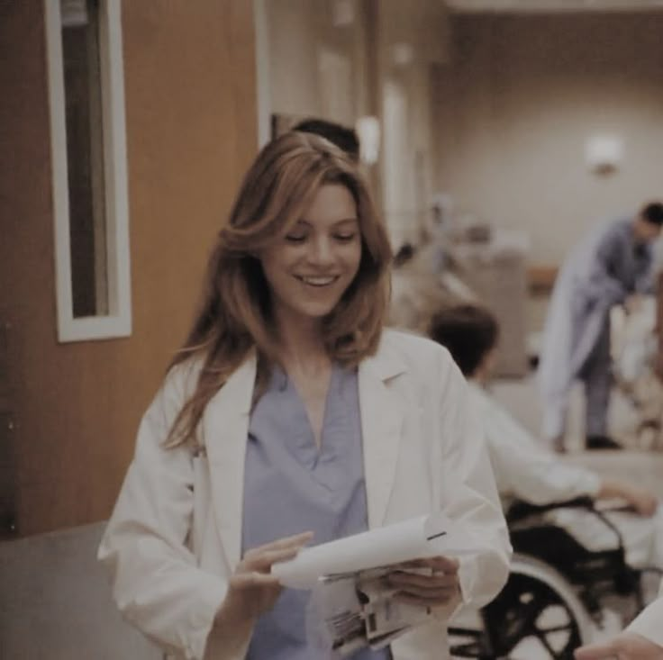 a woman in a white lab coat standing next to another woman holding papers and smiling