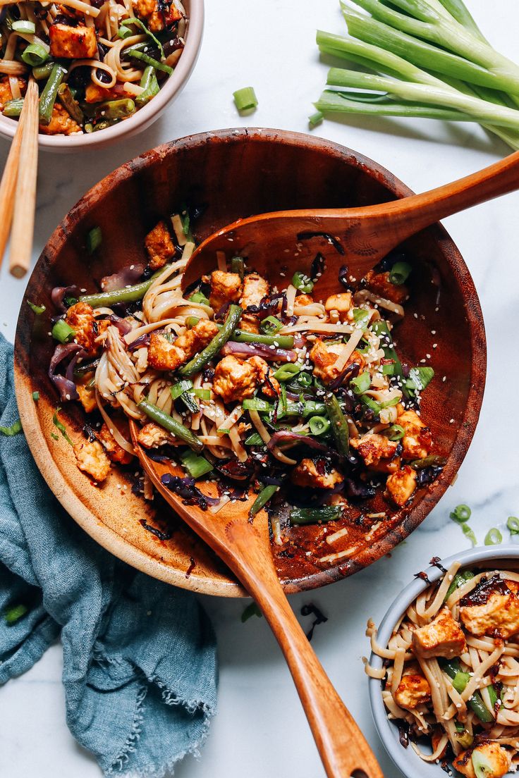 two wooden bowls filled with food next to green onions