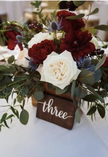 there is a vase filled with flowers and greenery on top of a white table