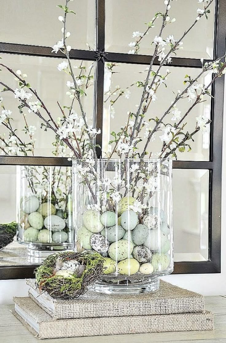 two vases filled with flowers and eggs sitting on top of books in front of a window