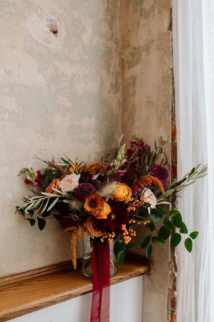 a bouquet of flowers sitting on top of a window sill next to a curtain