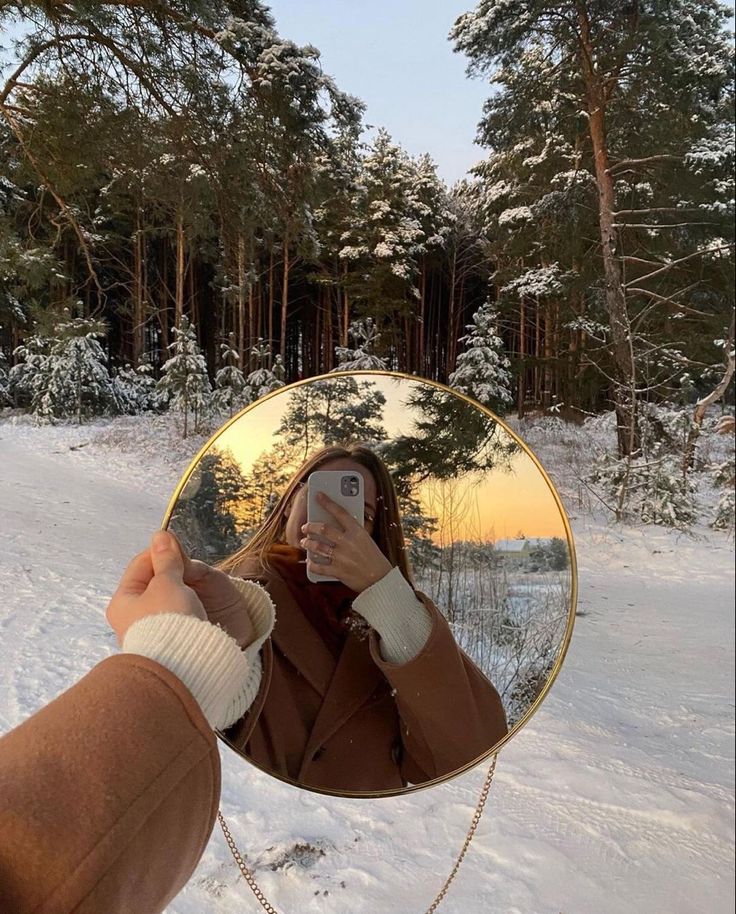 a woman taking a selfie in front of a round mirror on snow covered ground