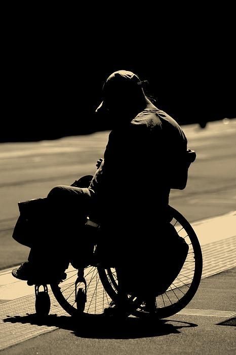 a person sitting in a wheel chair on the side of a road with their back to the camera