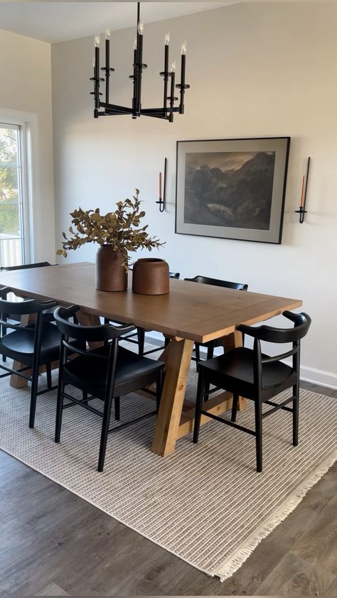 a dining room table with black chairs and a vase on top of it in front of a window