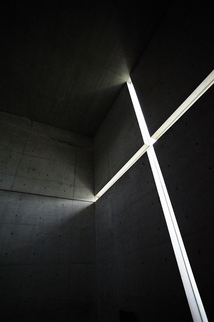 the light is shining through the cross in the dark room with concrete walls and floor