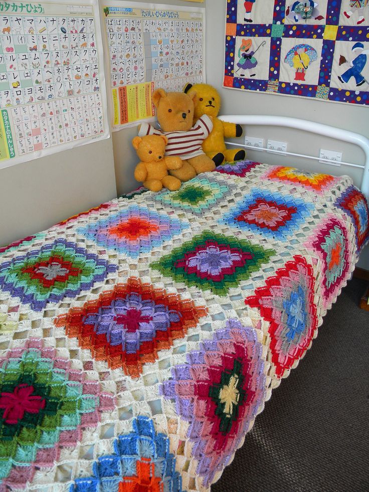 there is a crocheted blanket on the bed with teddy bears sitting on it