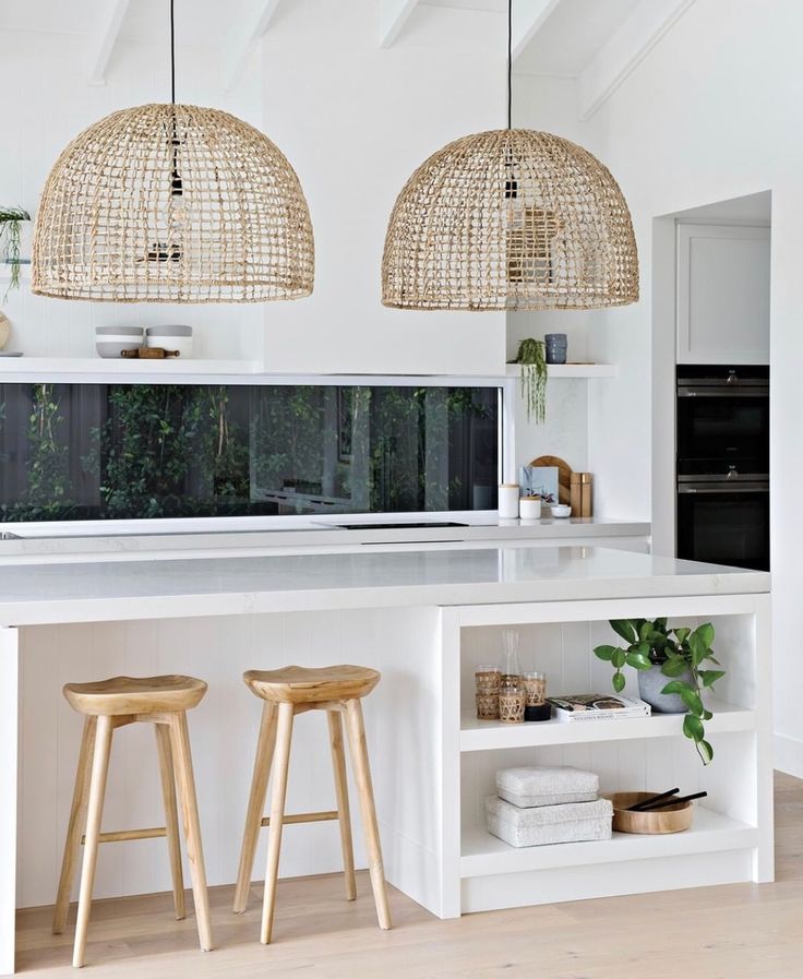 two wooden stools sit in front of an island with white countertops and pendant lights