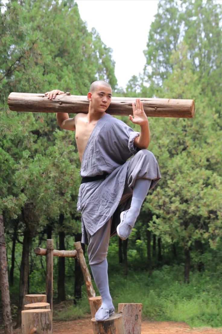 a man carrying a large log on his back while standing on logs in the woods