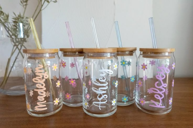 four personalized mason jars with straws and flowers on the lids, sitting on a table