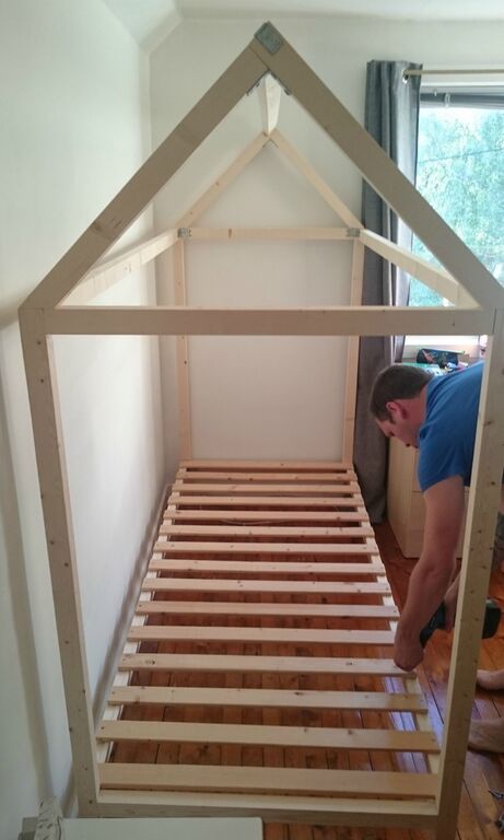 a man working on a bed frame in a room with hardwood floors and walls,