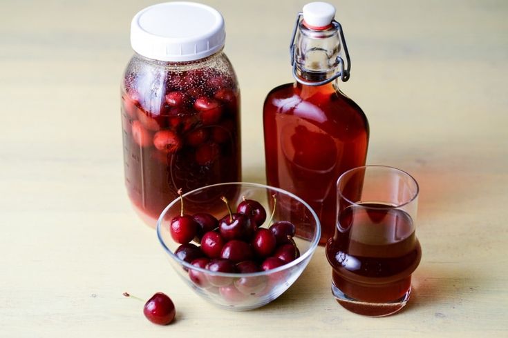 there is a glass bowl with cherries in it next to a bottle and two glasses