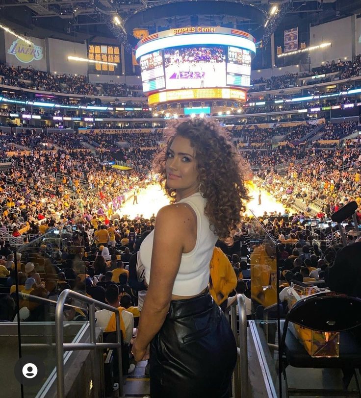 a woman standing in front of a crowd at a basketball game wearing black leather pants