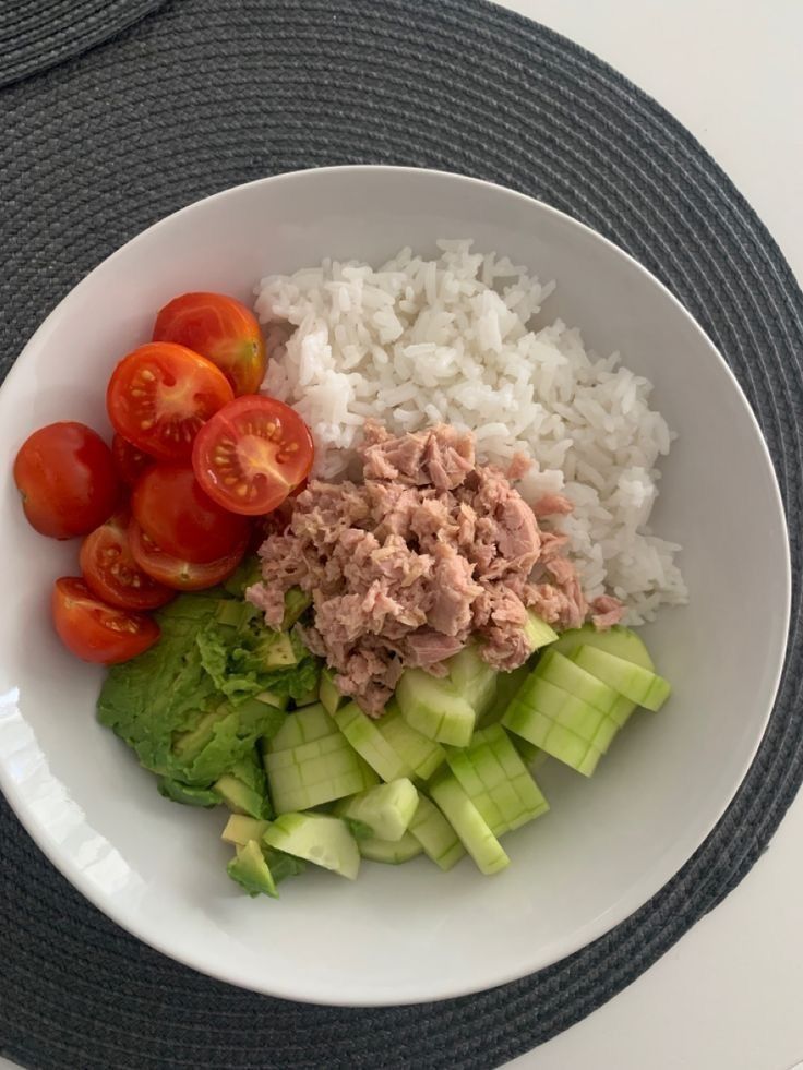 a white bowl filled with rice, cucumbers and tomatoes on top of a table