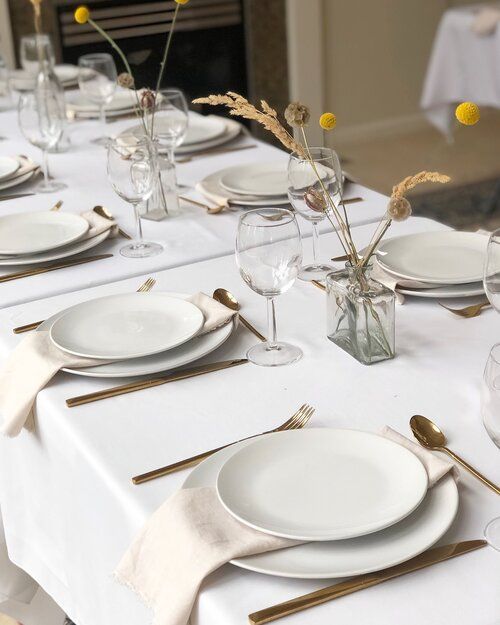 the table is set with white plates and silverware, gold cutlery, and yellow flowers