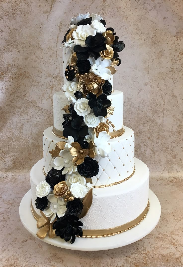 a three tiered wedding cake with black and white flowers on the top, gold trimmings