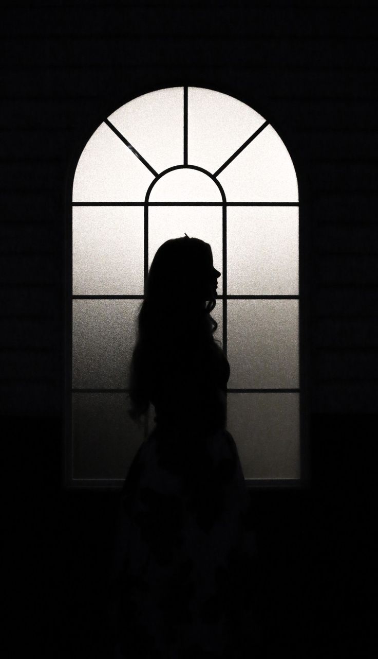 the silhouette of a person standing in front of a window with an arched glass pane