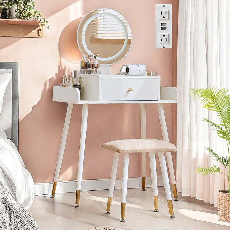 a white vanity table with a mirror and stool next to a plant on the floor