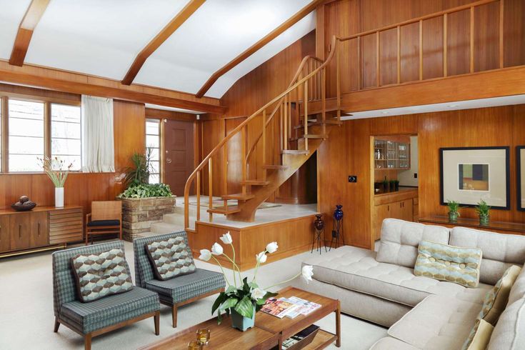 a living room filled with lots of furniture and wooden paneling on the walls next to a stair case