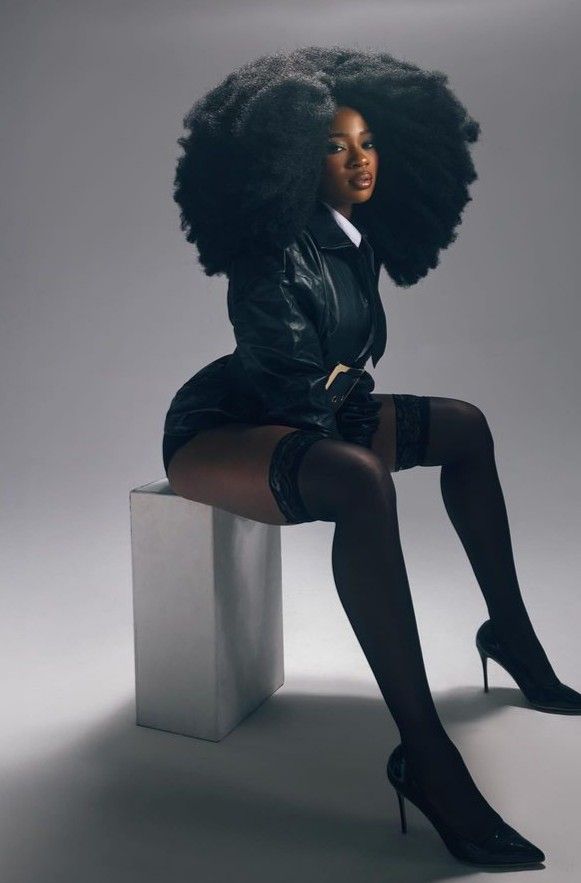 a woman sitting on top of a white block wearing black stockings and high heeled shoes