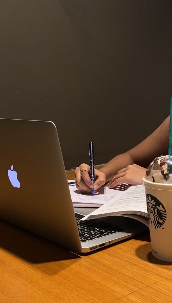 a person sitting at a table with a laptop and notebook in front of them, writing