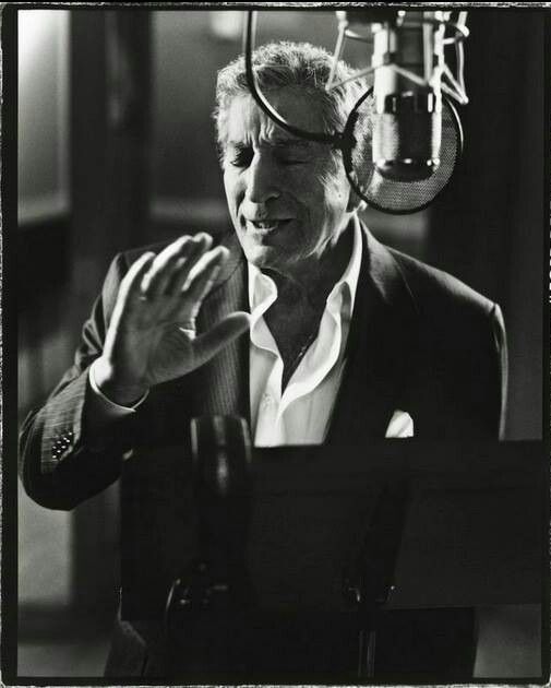 black and white photograph of man with headphones on in front of microphone, looking at camera