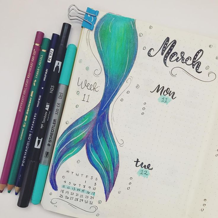 an open notebook with some markers and pencils next to it on a white surface