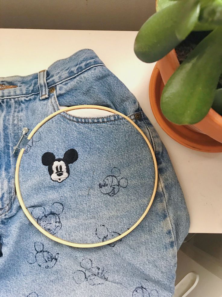 a mickey mouse embroidered on the back of a pair of jean shorts next to a potted plant