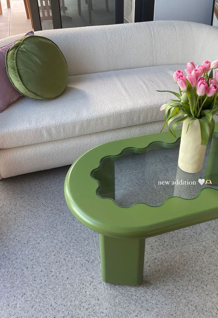 a green coffee table with pink flowers in a vase sitting on it's side