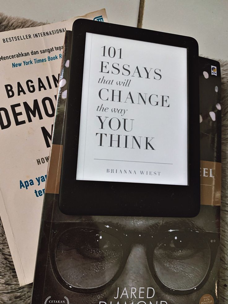 an electronic device sitting on top of a pile of books next to each other with glasses on it