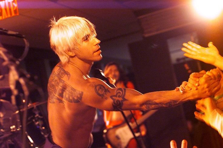 a man with white hair and tattoos on his arm reaching out to shake another person's hand