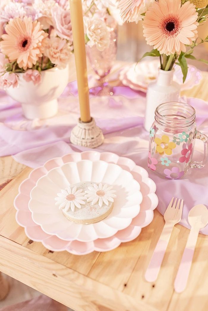 the table is set with pink and white plates, silver utensils and flowers in vases