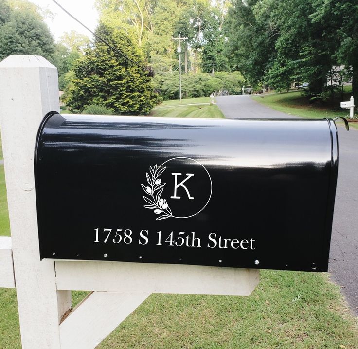 a black mailbox sitting on the side of a road next to a white fence