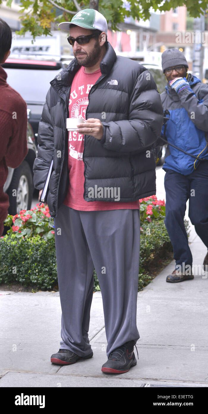 a man in a puffy jacket is standing on the sidewalk while looking at his cell phone