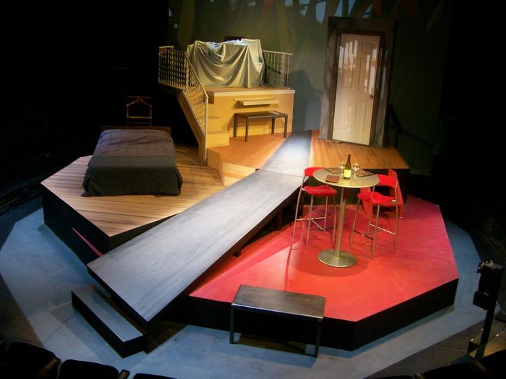 an empty stage with chairs and tables in the center, set up for a play