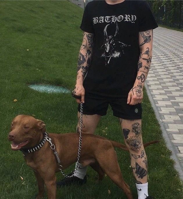 a man with tattoos on his arms and legs standing next to a brown dog wearing a chain