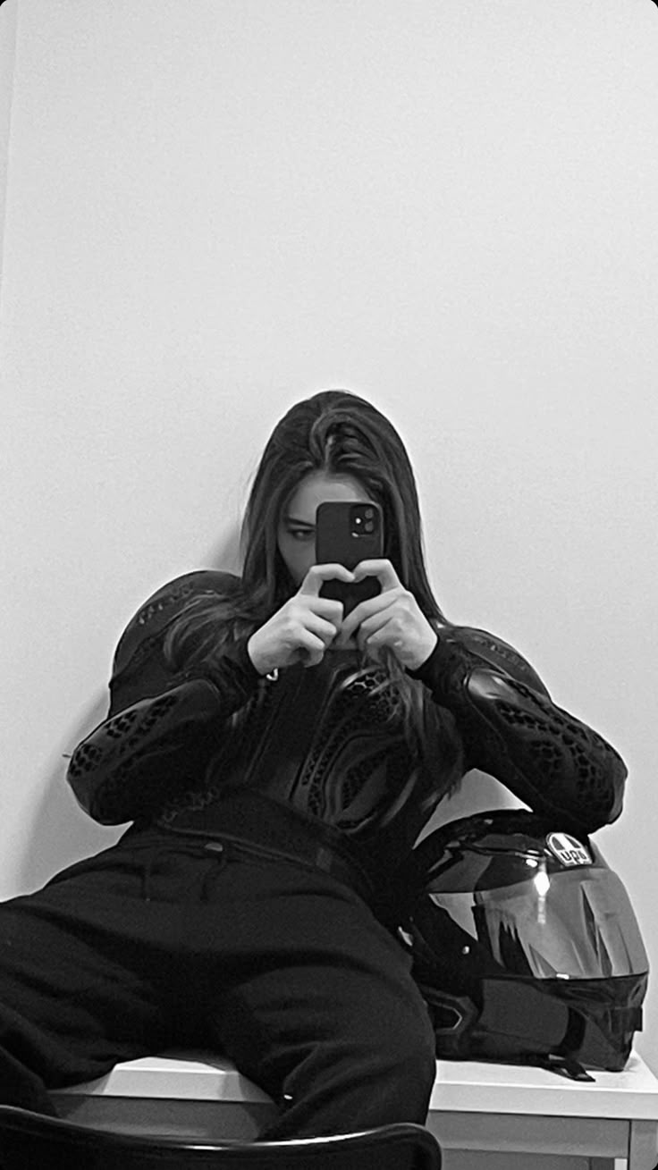 a woman taking a selfie in front of a motorcycle helmet while sitting on a chair