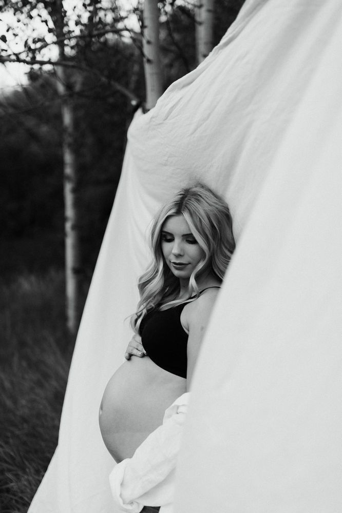 a pregnant woman leaning against a white sheet