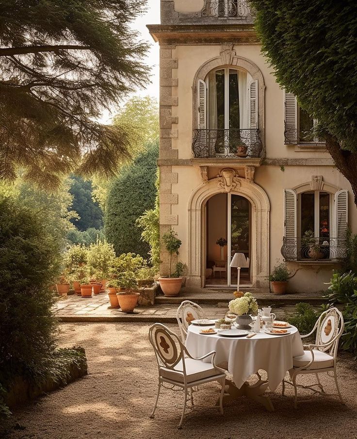 an outdoor dining table in front of a house with potted plants on the patio