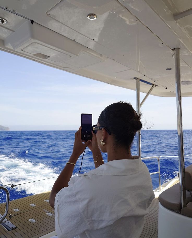 a woman taking a photo on her cell phone while sitting on a boat in the ocean