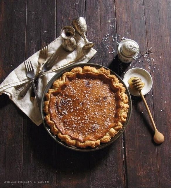 a pie sitting on top of a wooden table next to a fork and spoons