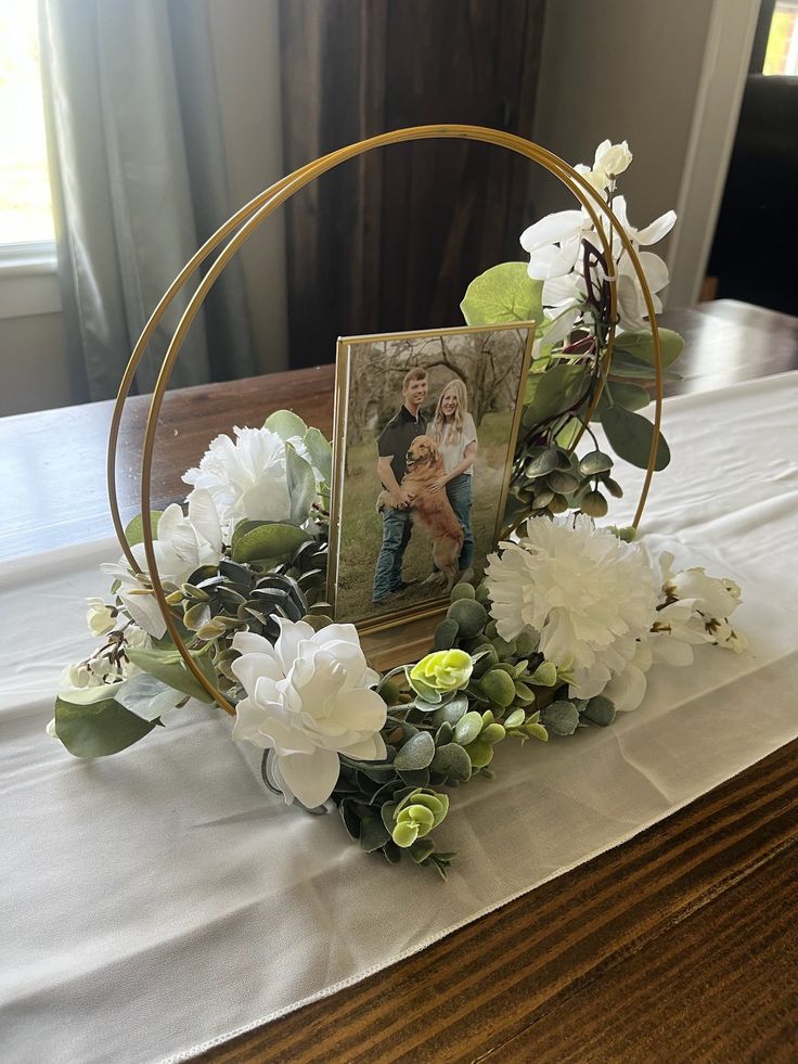 an arrangement of flowers and greenery on a table with a photo in the center