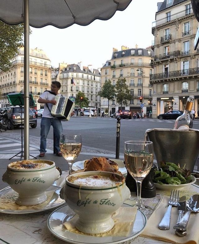 a table with food and wine on it in the middle of a city street, next to a man playing an accordion