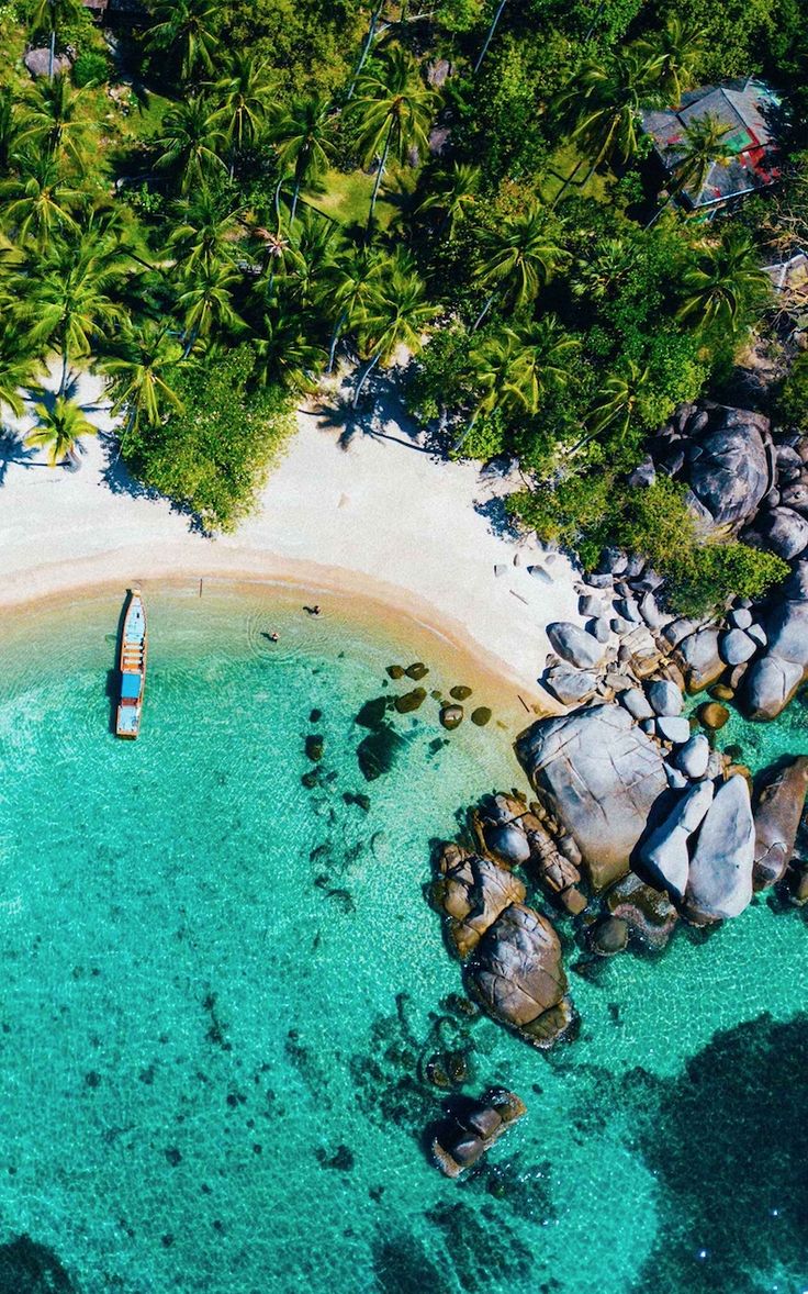 an aerial view of a boat on the water near some rocks and palm trees in the ocean