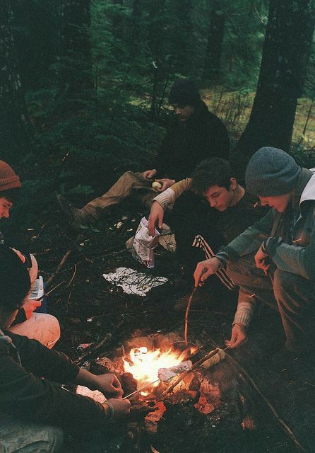 four people sitting around a campfire in the woods while one person lights a candle