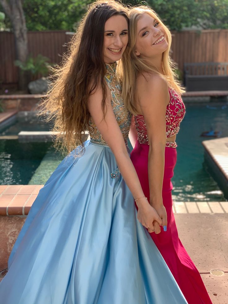 two young women in dresses standing next to each other near a pool and smiling at the camera