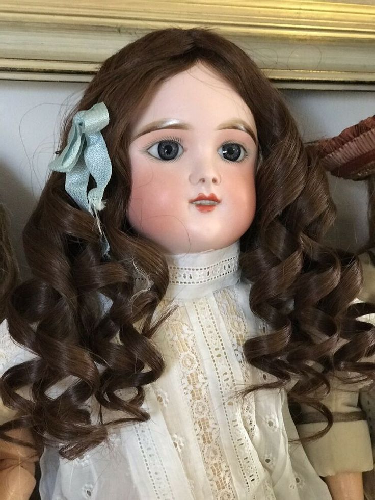 an old doll with long brown hair wearing a white dress and blue bow in her hair