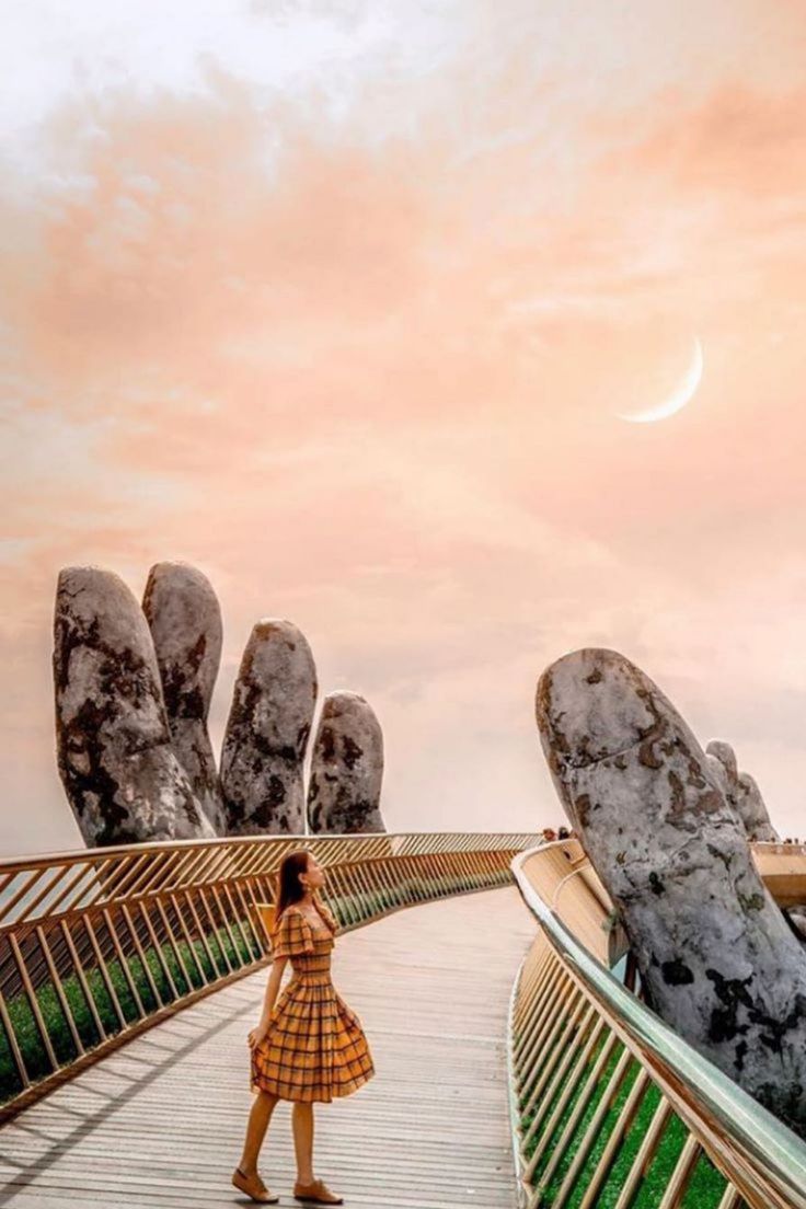 a woman standing on a bridge with two hands reaching for the sky in front of her